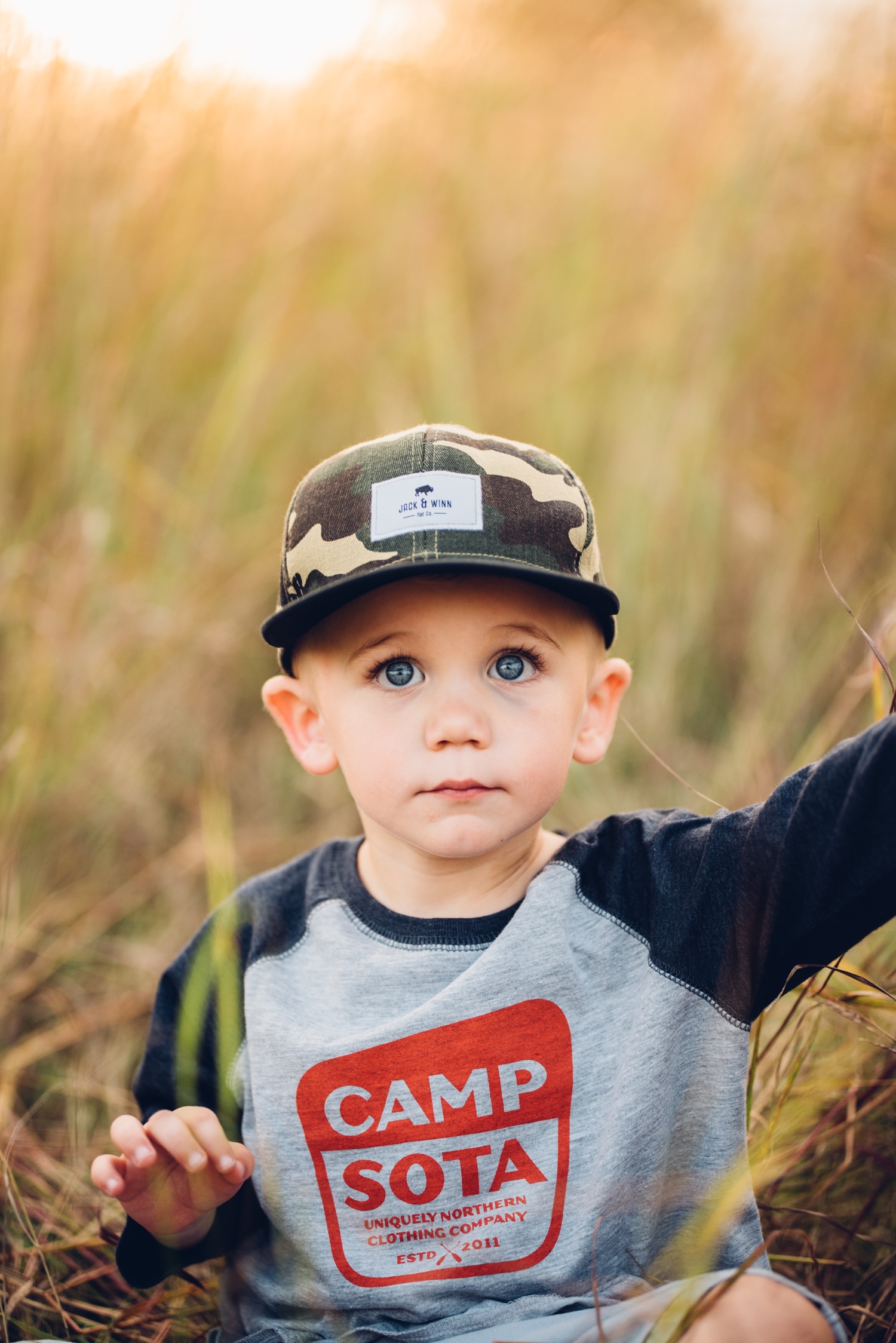 Toddler boy wearing Sota Clothing and Jack and Winn apparel in a field during minnesota family photo session.
